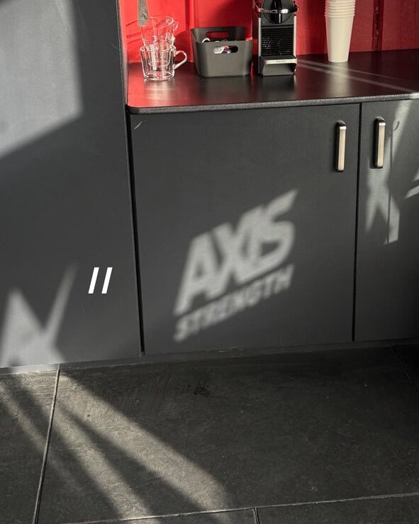 Inside the Axis studio, with the AXIS Strength logo projected onto the floor beside a rust-red wall