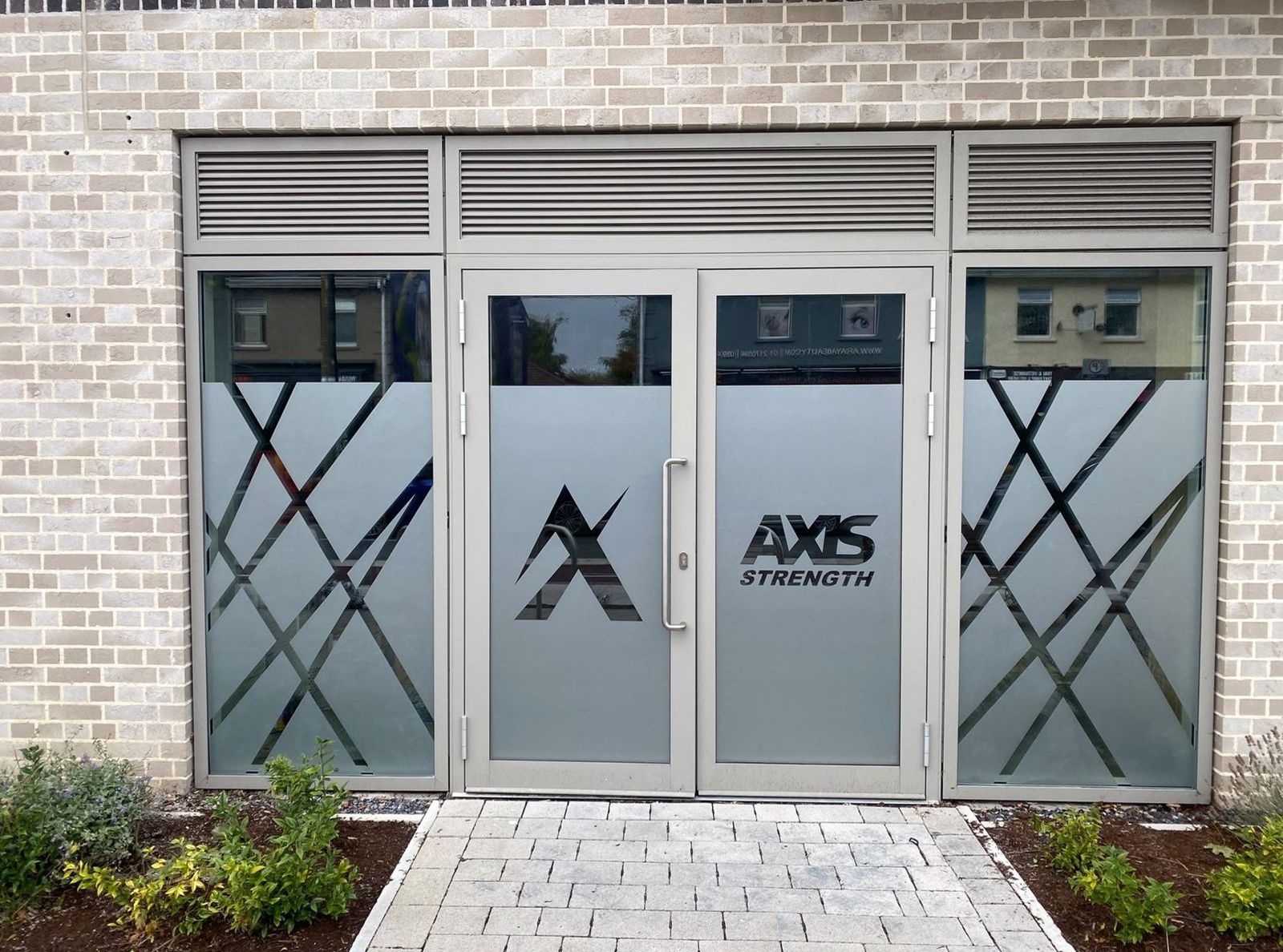 Axis shopfront with frosted vinyls showing the mark, the AXIS Strength wordmark and a crossed-line pattern