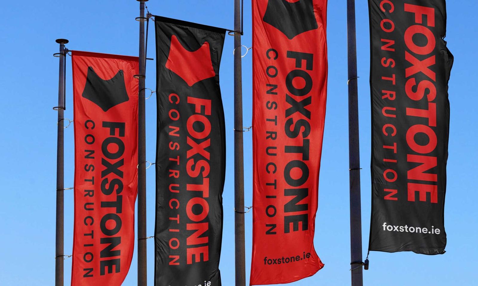 Red and black Foxstone Construction flags against a blue sky