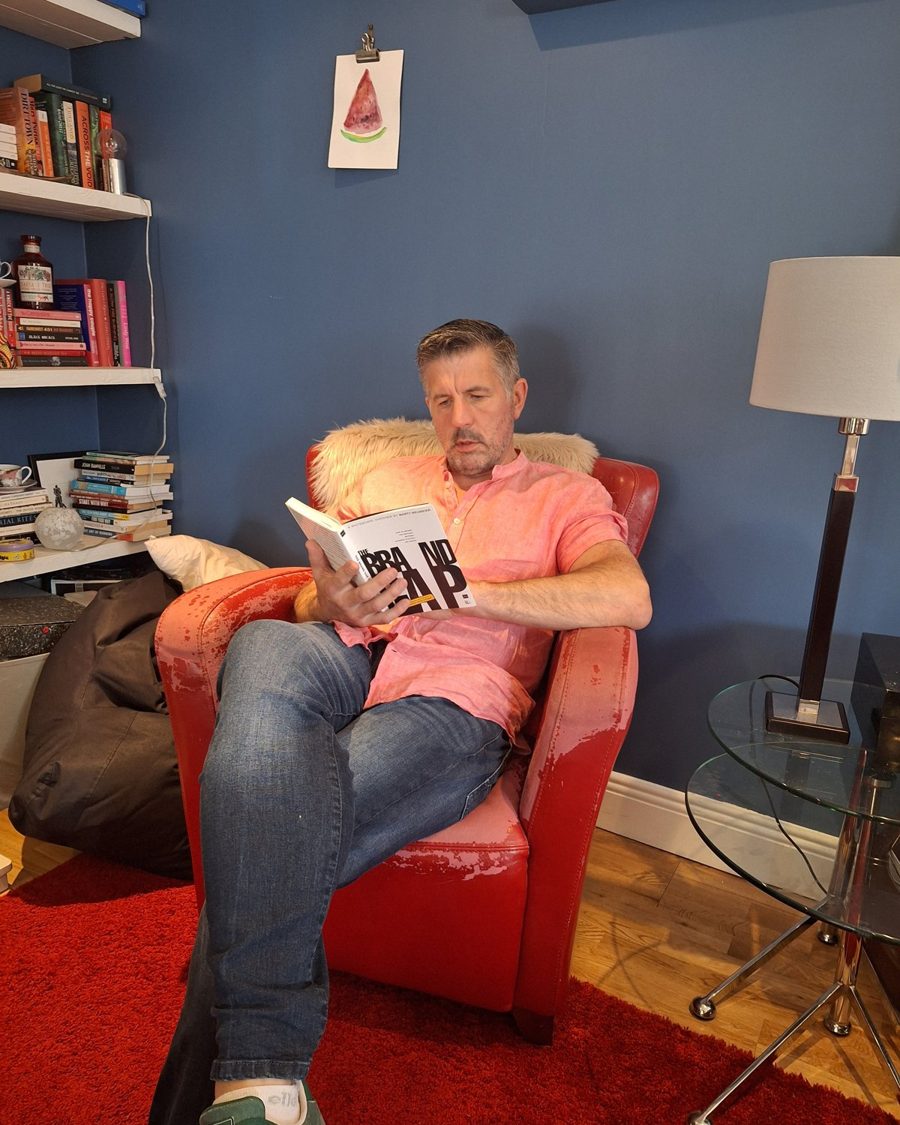 Barry O'Connor in a red armchair reading The Brand Gap